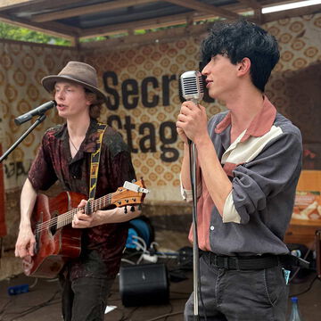 Duo mit Akustikgitarre und Retro-Mikrofon vor dem secret stage Schriftzug, Kieler Woche 2025