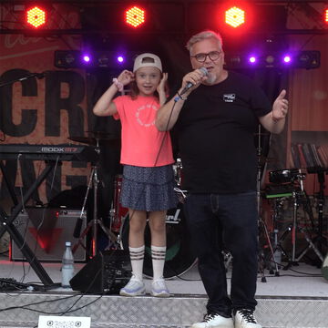 Musiker mit Mikrofon und ein Mädchen mit Basecap auf der Bühne der secret stage, Kieler Woche 2026