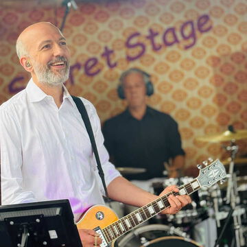 Gitarrist im weißen Hemd lächelt, im Hintergrund der Schlagzeuger, secret stage, Kieler Woche 2025