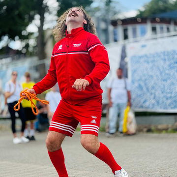 Straßenkünstler im roten Trainingsanzug mit Seil an der Kiellinie, Kiel Artist, Kieler Woche 2025