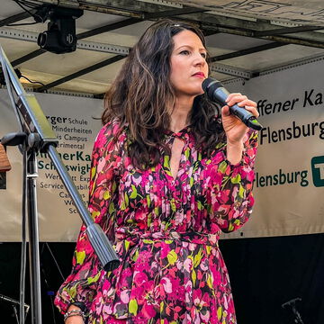 Sängerin im pinken Blumenkleid am Mikrofon auf der Bühne des Offenen Kanals, secret stage, Kieler Woche 2024