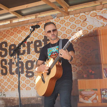 Gitarrist mit Sonnenbrille und Akustikgitarre vor dem secret stage Schriftzug, Kieler Woche 2025