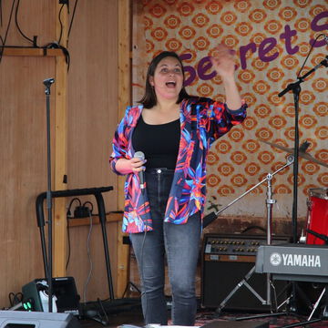Sängerin in bunter Jacke singt vor dem secret stage Schriftzug, Kieler Woche 2023